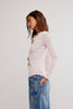 Woman wearing a light pink long-sleeve top and blue jeans against a white background