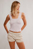 Woman wearing a light pink sleeveless top and beige shorts on a plain background